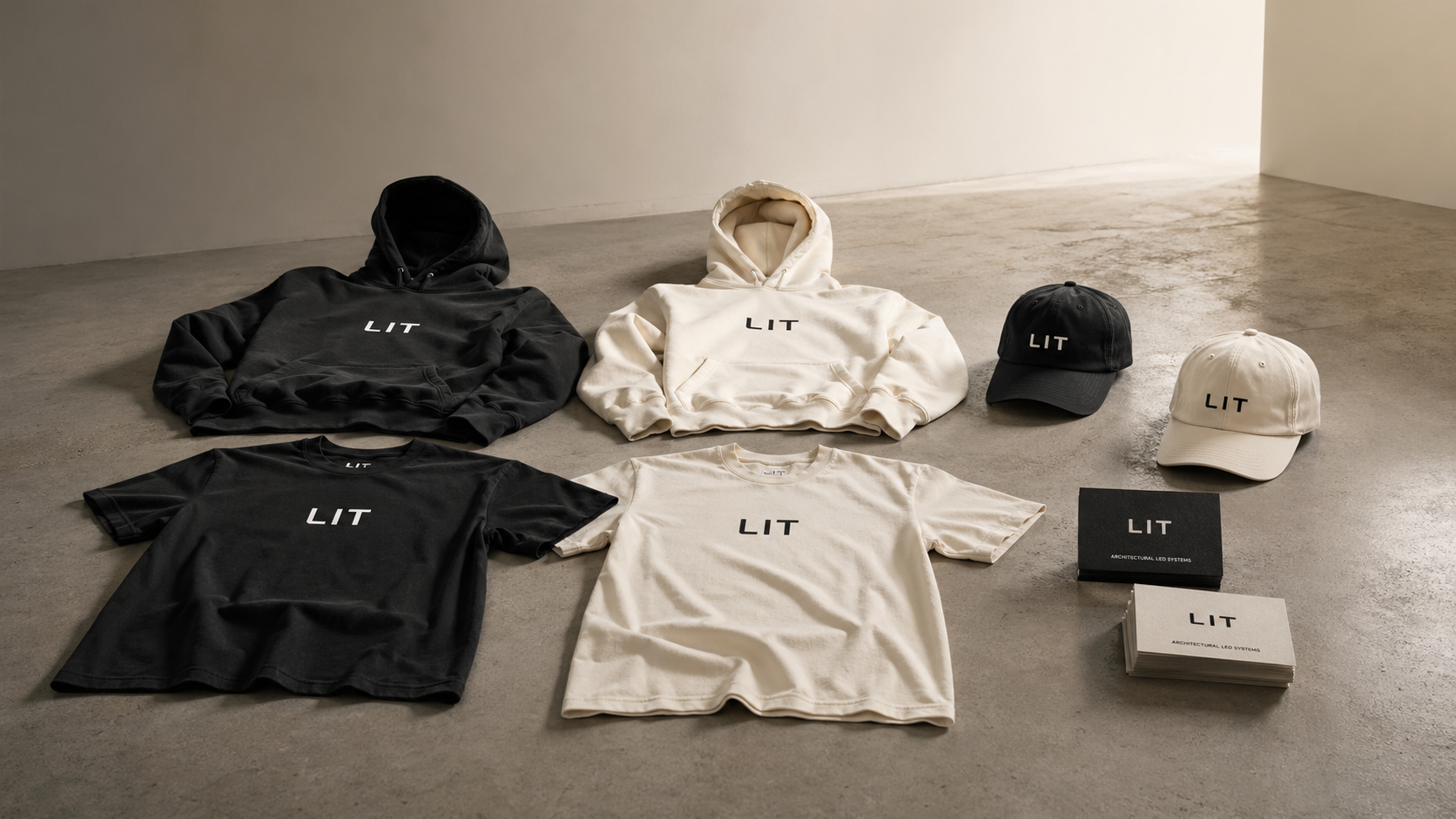 Lit Group merch collection &mdash; hoodies, t-shirts, caps, and business cards laid out on a concrete studio floor.